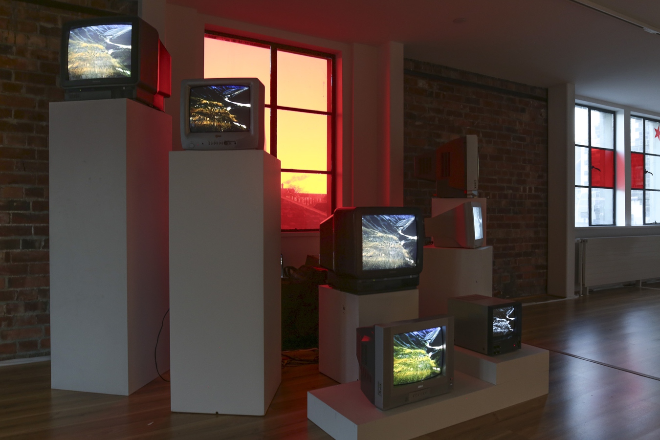 Install view of CRT monitors playing video with red light from behind.