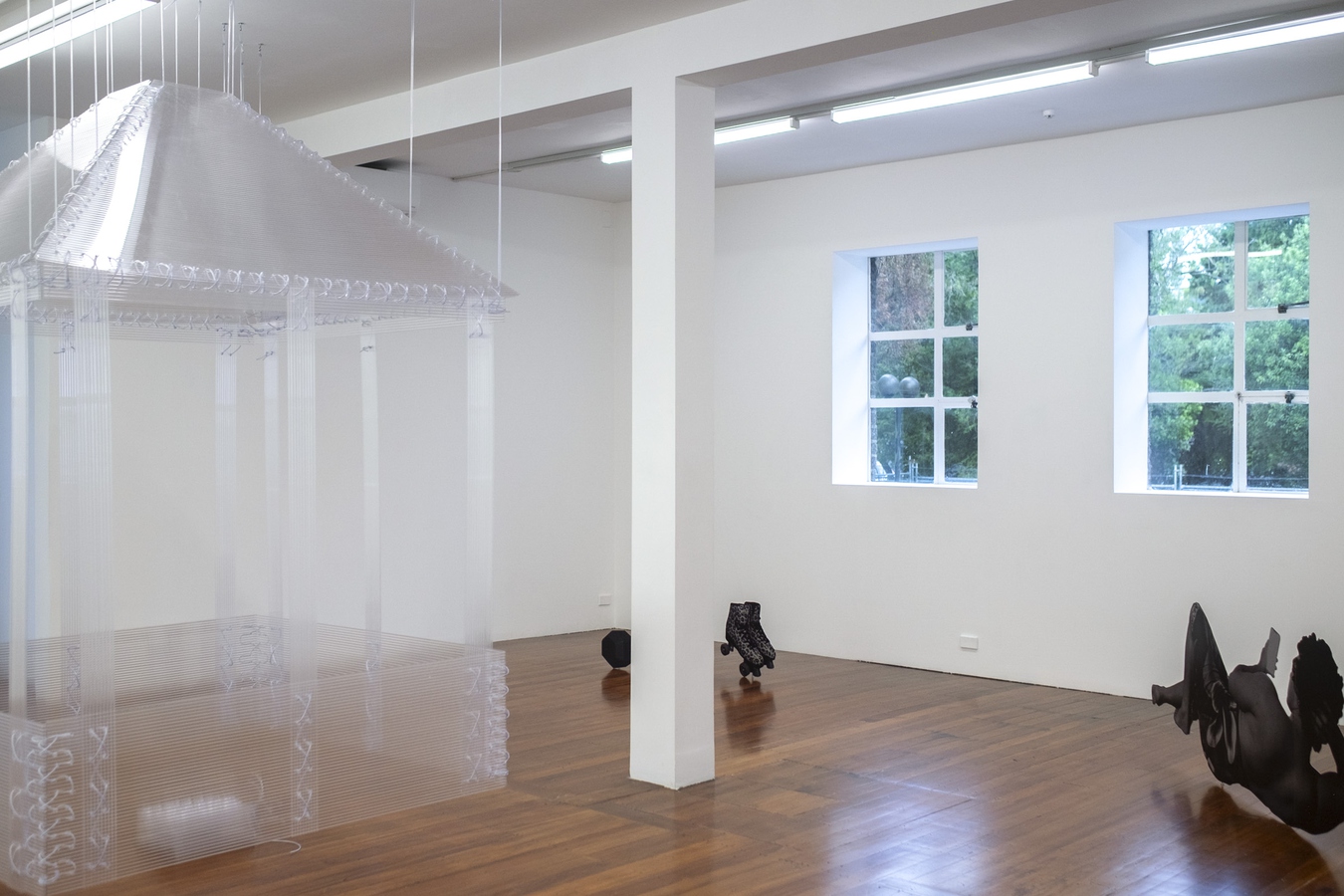 Image of the gallery space with two large sculptural works, a transparent fale and metal silhouette of a figure