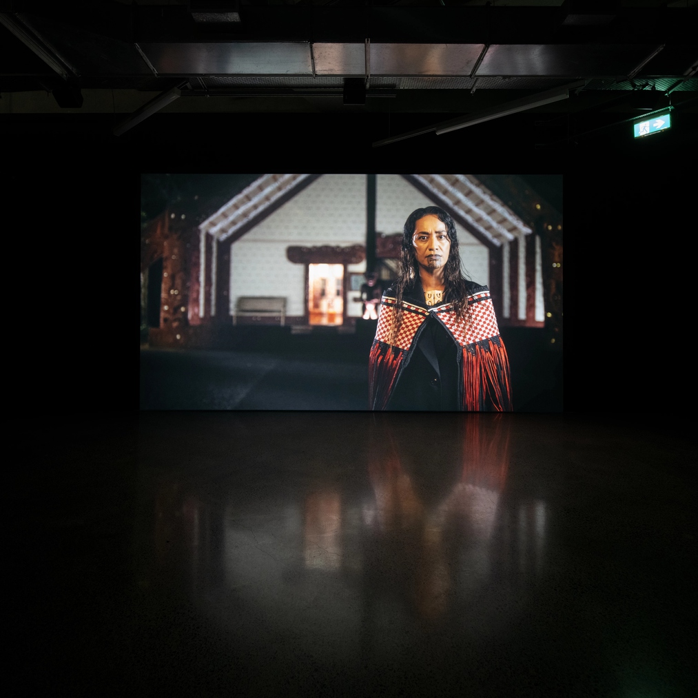 colour photograph of the installation of work whakakmoemoea, in black galley, Oriini Kaipara stands in front of Waitangi marae